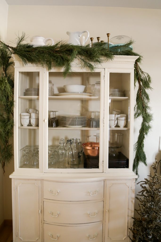 Simple green garland on the china hutch, and a gold christmas tree decorate the farmhouse for Christmas.