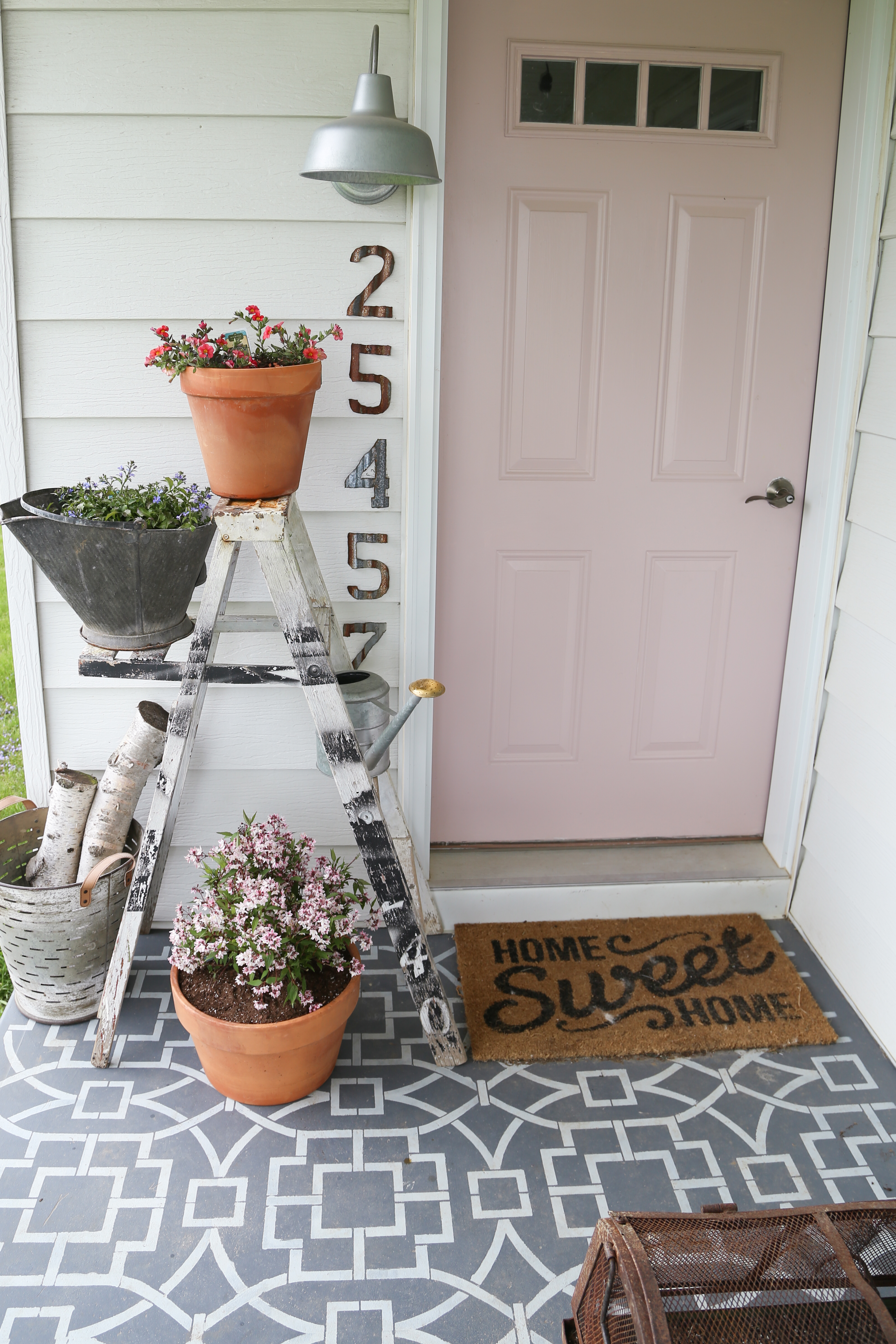 The pink and purple farmhouse front porch with blush front door, tiled cement flooring, colorful flowers and rusty accents.