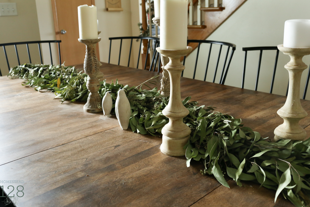 Clean and modern farmhouse Christmas table is draped with a eucalyptus and olive leaf garland and large white candles.